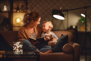 Maman et son enfant lisant à la lumière d'une lampe dans leur salon - la bellenergie